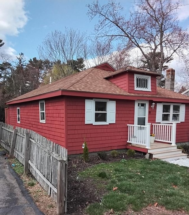 view of front of house with roof with shingles, a front lawn, fence, and a chimney