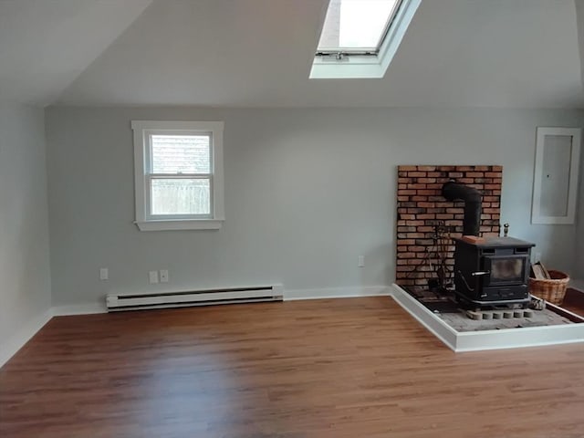 unfurnished living room with vaulted ceiling with skylight, a wood stove, baseboard heating, wood finished floors, and baseboards