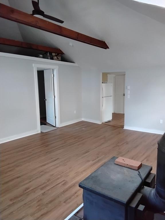 unfurnished living room with ceiling fan, wood finished floors, lofted ceiling with beams, and baseboards