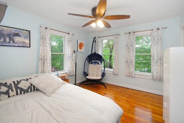 bedroom with multiple windows, wood finished floors, baseboards, and ceiling fan