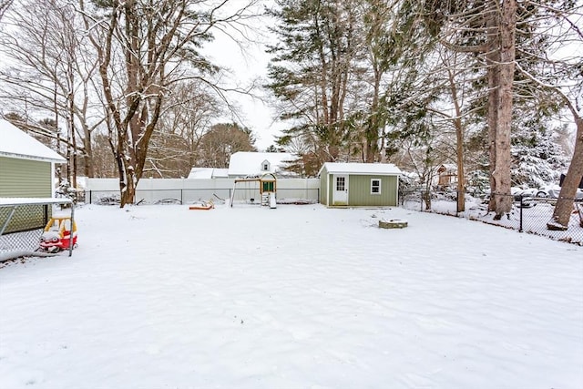 snowy yard with a playground and a storage shed