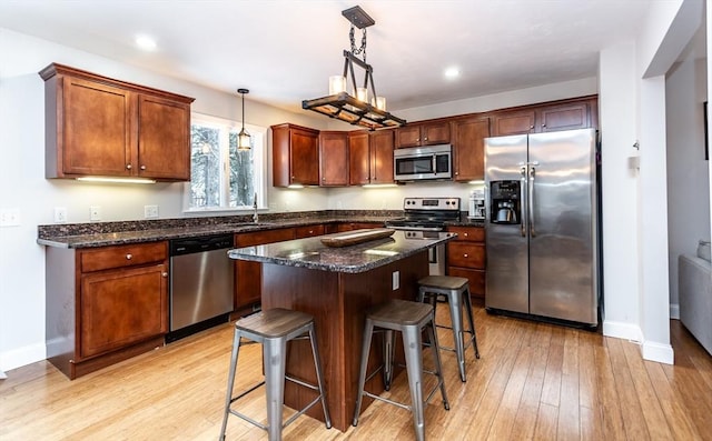 kitchen with appliances with stainless steel finishes, a center island, a kitchen bar, hanging light fixtures, and light wood-type flooring