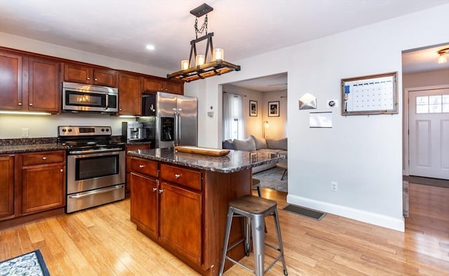 kitchen with appliances with stainless steel finishes, a kitchen breakfast bar, light wood-type flooring, hanging light fixtures, and a center island