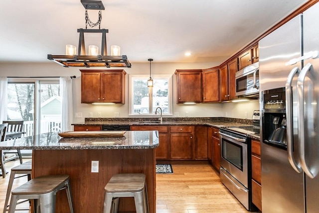 kitchen with dark stone countertops, pendant lighting, sink, a kitchen breakfast bar, and stainless steel appliances