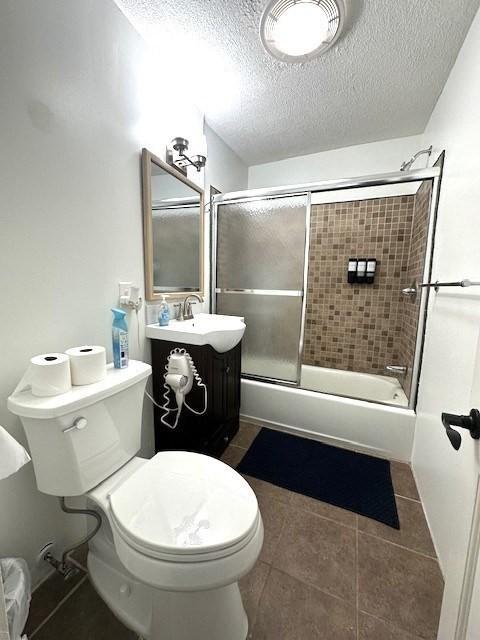 bathroom with tile patterned floors, a textured ceiling, toilet, and shower / bath combination with glass door