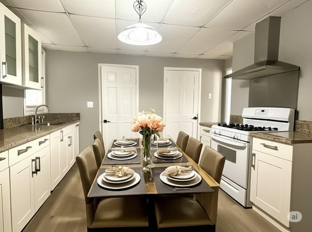 kitchen with a sink, wall chimney range hood, wood finished floors, white gas range oven, and a drop ceiling