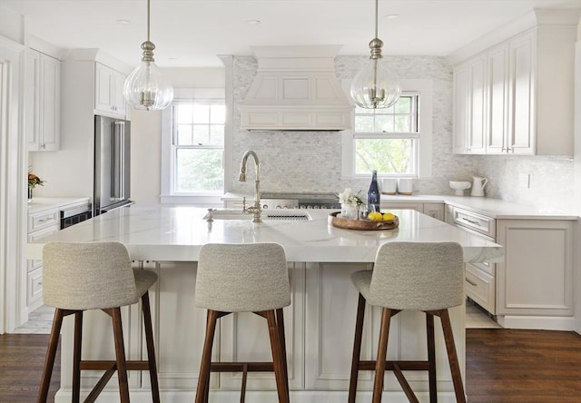 kitchen featuring stainless steel fridge, a kitchen island with sink, sink, and decorative light fixtures