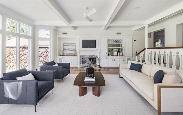 living room featuring a high end fireplace, light wood-type flooring, coffered ceiling, ceiling fan, and beam ceiling