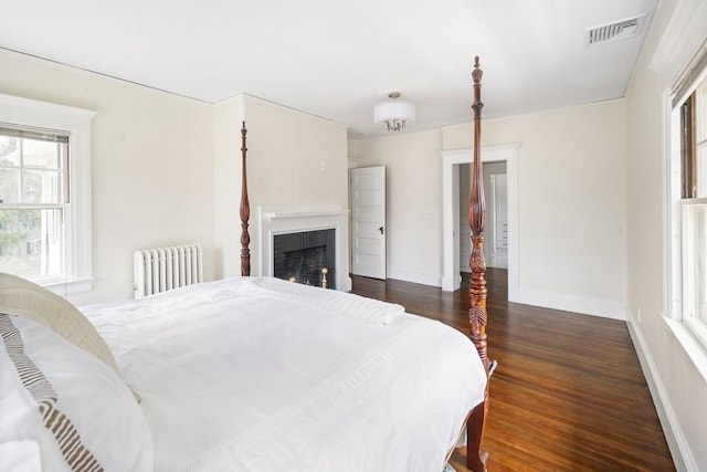 bedroom featuring radiator heating unit, a brick fireplace, and dark wood-type flooring