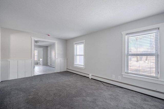 carpeted empty room with a baseboard heating unit and a textured ceiling