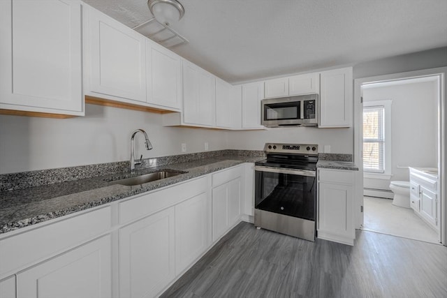 kitchen featuring sink, baseboard heating, dark hardwood / wood-style flooring, stainless steel appliances, and white cabinets