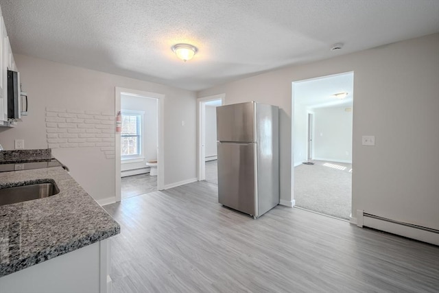 kitchen featuring stainless steel refrigerator, a baseboard heating unit, a textured ceiling, and white cabinets