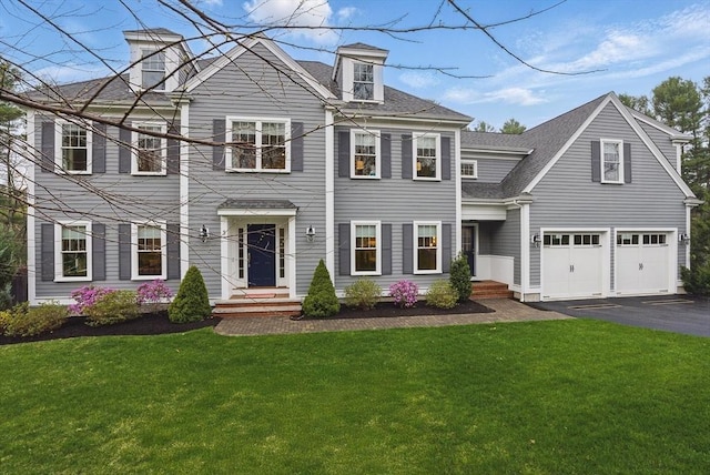 colonial-style house with a garage, aphalt driveway, roof with shingles, and a front yard