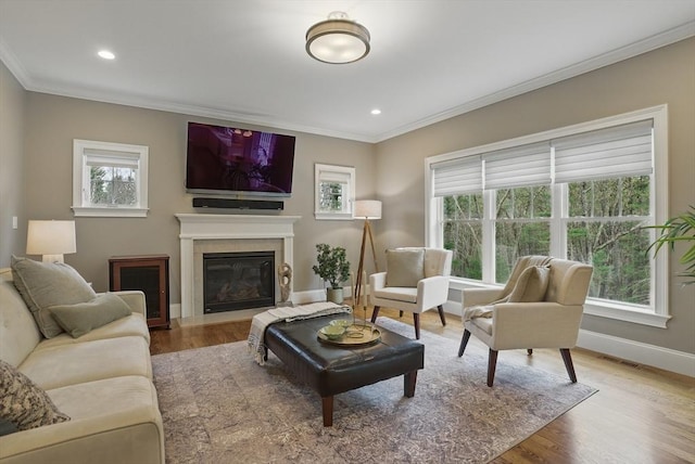 living area featuring baseboards, a fireplace with flush hearth, ornamental molding, and visible vents