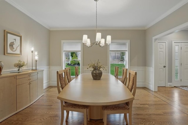 dining space featuring light wood finished floors, a wainscoted wall, and a notable chandelier