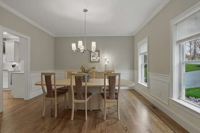 dining area featuring ornamental molding, wainscoting, light wood-type flooring, and a chandelier