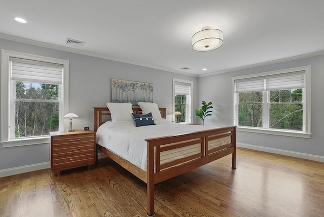 bedroom with baseboards, ornamental molding, wood finished floors, and visible vents