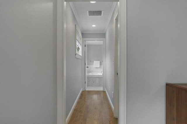 hallway featuring crown molding, baseboards, wood finished floors, and visible vents