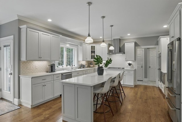 kitchen with light countertops, stainless steel appliances, ornamental molding, and wall chimney exhaust hood