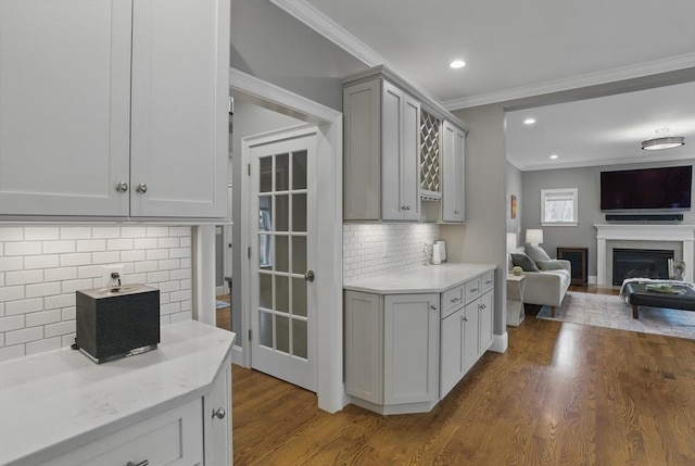 kitchen with decorative backsplash, a fireplace, wood finished floors, open floor plan, and ornamental molding