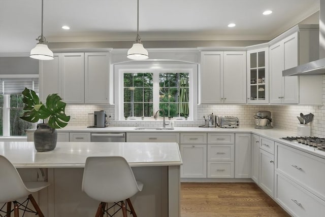 kitchen featuring wall chimney range hood, crown molding, a breakfast bar area, and a sink