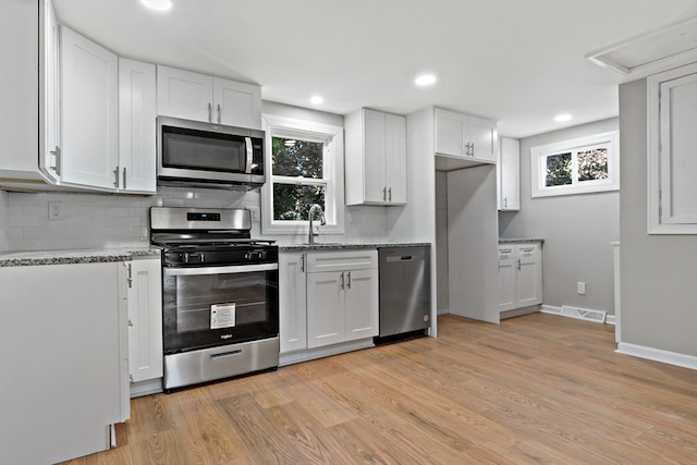 kitchen with light wood-type flooring, white cabinetry, backsplash, light stone counters, and appliances with stainless steel finishes