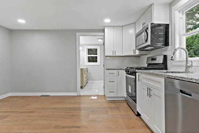 kitchen with white cabinets, light stone countertops, stainless steel appliances, light hardwood / wood-style floors, and sink