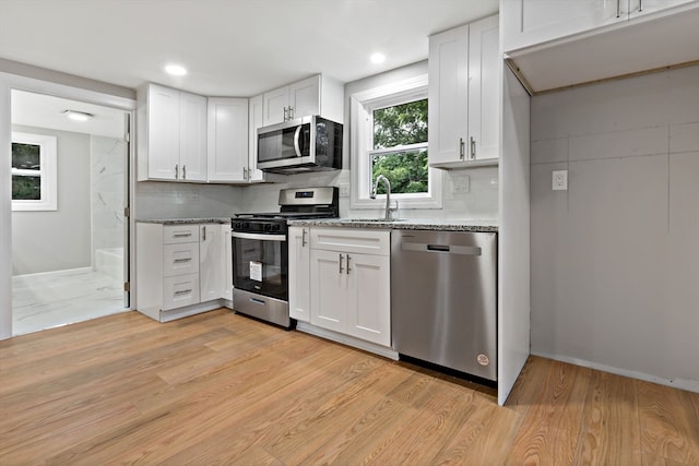 kitchen with stainless steel appliances, light stone counters, white cabinets, and light hardwood / wood-style floors