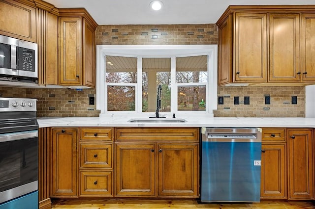 853 Oxford St S, Auburn, MA 01501 - kitchen with stainless steel appliances, a sink, brown cabinetry, decorative backsplash, and light wood-type flooring