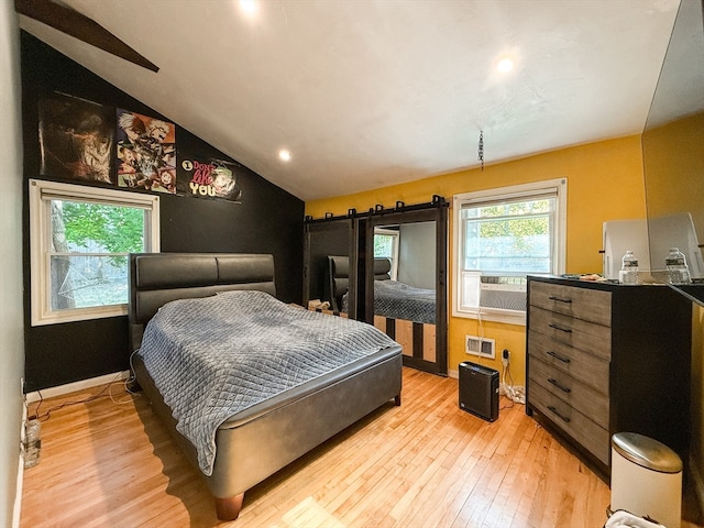 bedroom featuring light hardwood / wood-style floors, cooling unit, a barn door, and vaulted ceiling