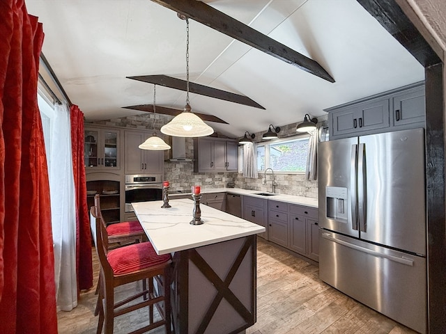 kitchen featuring a kitchen island, vaulted ceiling with beams, stainless steel appliances, sink, and pendant lighting