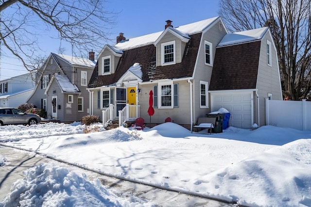 colonial inspired home with a garage, roof with shingles, fence, and a gambrel roof