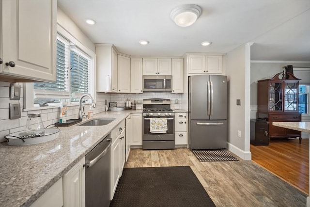 kitchen featuring light wood finished floors, tasteful backsplash, stainless steel appliances, white cabinetry, and a sink