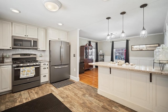 kitchen featuring appliances with stainless steel finishes, light stone counters, crown molding, white cabinetry, and pendant lighting