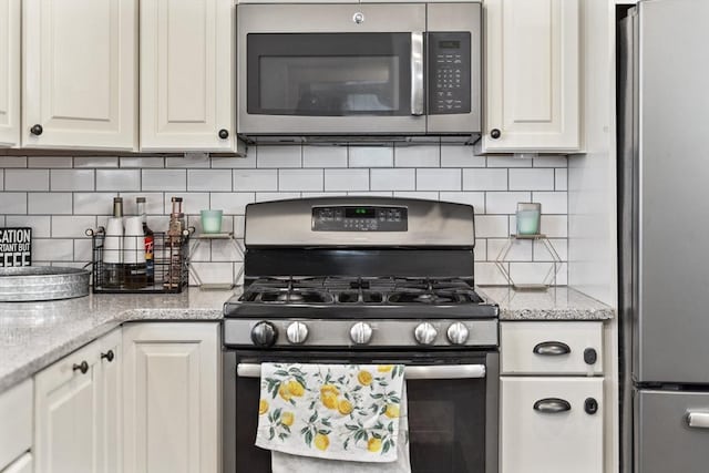 kitchen featuring appliances with stainless steel finishes, decorative backsplash, light stone counters, and white cabinets