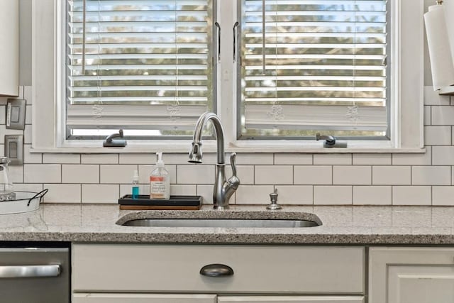 details with white cabinetry, a sink, stainless steel dishwasher, and light stone countertops