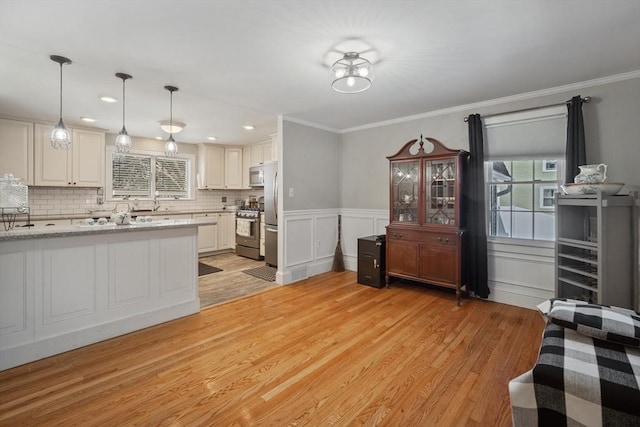 kitchen featuring light stone counters, stainless steel appliances, crown molding, light wood-style floors, and pendant lighting