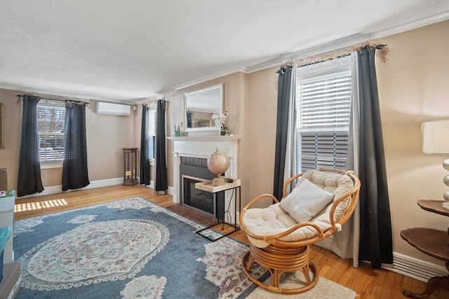 living area with light wood-style flooring, a wall mounted AC, a fireplace with flush hearth, ornamental molding, and baseboards