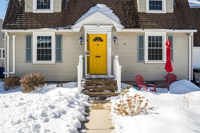 snow covered property entrance featuring a shingled roof