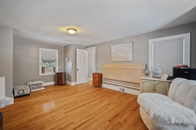 living area featuring light wood-style floors, visible vents, baseboards, and cooling unit