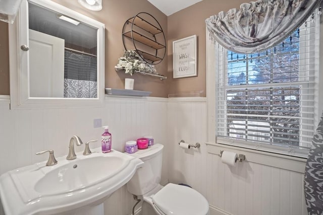 bathroom with toilet, a shower with curtain, a sink, and wainscoting