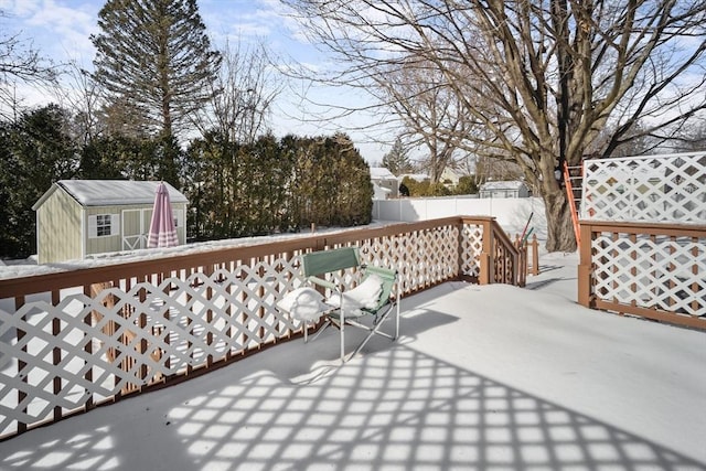 snow covered deck with an outbuilding, a fenced backyard, and a storage shed