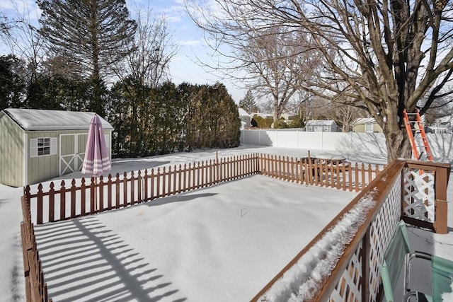 snow covered deck featuring a fenced backyard, an outdoor structure, and a storage shed