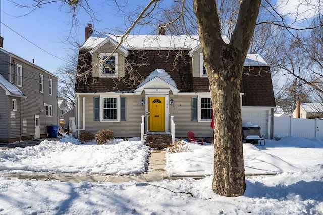 colonial inspired home with an attached garage, a chimney, fence, and roof with shingles