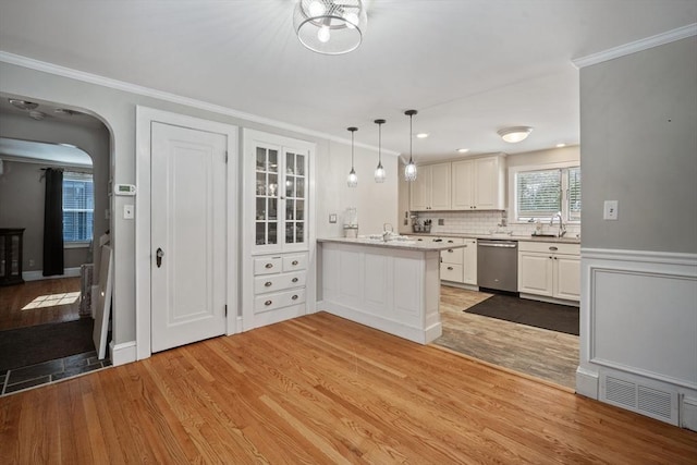 kitchen featuring a peninsula, white cabinetry, light countertops, stainless steel dishwasher, and pendant lighting