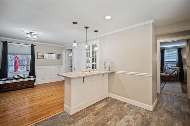 kitchen with ornamental molding, a kitchen breakfast bar, wood finished floors, hanging light fixtures, and a peninsula