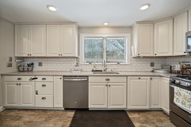 kitchen with appliances with stainless steel finishes, white cabinetry, a sink, and light stone countertops