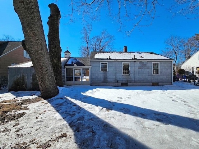 snow covered property with a sunroom, fence, and a chimney