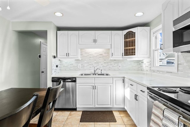 kitchen with a sink, white cabinetry, stainless steel appliances, light tile patterned flooring, and glass insert cabinets