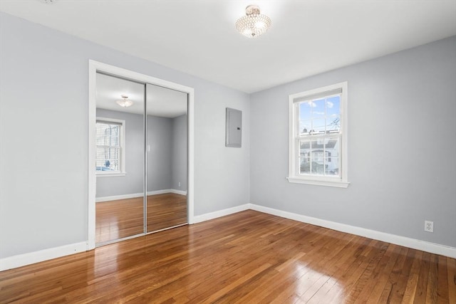 unfurnished bedroom featuring hardwood / wood-style flooring, electric panel, baseboards, and a closet